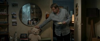 Movie still from “Graduation” (2016), directed by Cristian Mungiu – A man holding a plate in front of a teddy bear; Medium shot, Over the shoulder angle