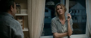 Movie still from “Graduation” (2016), directed by Cristian Mungiu – A woman standing in front of a window looking sad; Medium shot, Over the shoulder angle