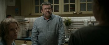 Movie still from “Graduation” (2016), directed by Cristian Mungiu – A man standing in a kitchen looking at the camera; Medium shot, Over the shoulder angle