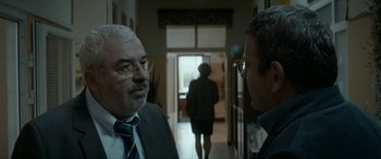 Movie still from “Graduation” (2016), directed by Cristian Mungiu – Two men in suits talking in front of a door; Medium shot, Over the shoulder angle