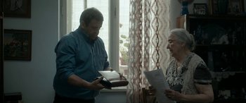Movie still from “Graduation” (2016), directed by Cristian Mungiu – An older man and a younger woman looking at a book; Medium shot, Over the shoulder angle