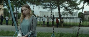 Movie still from “Graduation” (2016), directed by Cristian Mungiu – A girl is sitting on a swing in a park; Medium shot, Over the shoulder angle