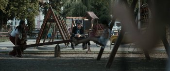 Movie still from “Graduation” (2016), directed by Cristian Mungiu – A man sitting on a bench in front of a girl swinging a swing; Wide shot, Over the shoulder angle