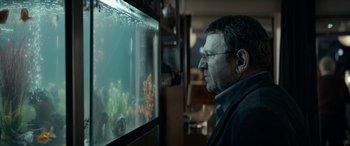 Movie still from “Graduation” (2016), directed by Cristian Mungiu – A man looking at a fish tank in a living room; Close Up shot, Over the shoulder angle