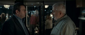 Movie still from “Graduation” (2016), directed by Cristian Mungiu – Two people are talking in front of a glass wall; Medium shot, Over the shoulder angle