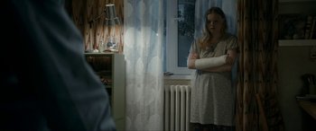 Movie still from “Graduation” (2016), directed by Cristian Mungiu – A woman standing in a room with a broken arm in a cast; Medium shot, Over the shoulder angle
