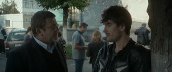 Movie still from “Graduation” (2016), directed by Cristian Mungiu – Two men standing next to each other on a sidewalk; Medium shot, Over the shoulder angle