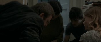 Movie still from “Graduation” (2016), directed by Cristian Mungiu – A group of people standing around each other in a room; Medium shot, High angle