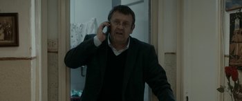 Movie still from “Graduation” (2016), directed by Cristian Mungiu – A man talking on a cell phone while wearing a suit; Medium shot, Low angle
