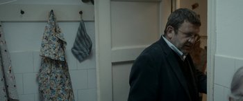 Movie still from “Graduation” (2016), directed by Cristian Mungiu – A man standing in front of a bathroom stall; Medium shot, Over the shoulder angle