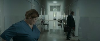 Movie still from “Graduation” (2016), directed by Cristian Mungiu – A woman in a blue gown and a man in a black suit walking down a hall way; Wide shot, High angle