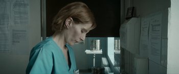 Movie still from “Graduation” (2016), directed by Cristian Mungiu – A woman in a blue lab coat looking out a window; Close Up shot, Low angle