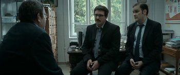 Movie still from “Graduation” (2016), directed by Cristian Mungiu – A man in a suit sitting in front of a desk; Medium shot, Over the shoulder angle