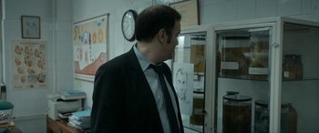 Movie still from “Graduation” (2016), directed by Cristian Mungiu – A man wearing a suit and tie standing in front of a drawing; Medium shot, Over the shoulder angle