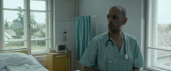 Movie still from “Graduation” (2016), directed by Cristian Mungiu – A man with a stethoscope standing in front of a mirror; Medium shot, Low angle