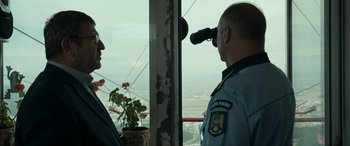 Movie still from “Graduation” (2016), directed by Cristian Mungiu – A man looking out of a window at a view of a city; Medium shot, Low angle