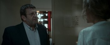 Movie still from “Graduation” (2016), directed by Cristian Mungiu – A man standing in front of a wall with papers on the wall; Close Up shot, Over the shoulder angle