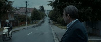 Movie still from “Graduation” (2016), directed by Cristian Mungiu – A man standing on the side of a road; Medium shot, Over the shoulder angle