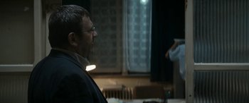Movie still from “Graduation” (2016), directed by Cristian Mungiu – A man with glasses is looking at a woman in a dark room; Medium shot, Over the shoulder angle