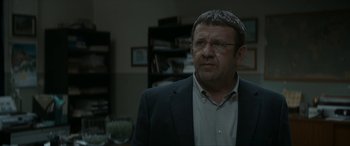 Movie still from “Graduation” (2016), directed by Cristian Mungiu – A man in a suit and glasses looking at the camera; Close Up shot, Over the shoulder angle