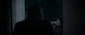Movie still from “Graduation” (2016), directed by Cristian Mungiu – A man in a black suit is standing in the dark; Medium shot, Over the shoulder angle