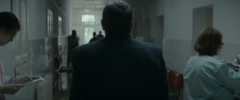 Movie still from “Graduation” (2016), directed by Cristian Mungiu – A man wearing a suit and tie in a room; Medium shot, Over the shoulder angle