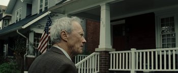 Movie still from “Gran Torino” (2008), directed by Clint Eastwood – An older man wearing a suit and tie outside of a house; Close Up shot, Over the shoulder angle
