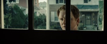 Movie still from “Gran Torino” (2008), directed by Clint Eastwood – A man looking out of a window at a neighborhood; Close Up shot, Over the shoulder angle
