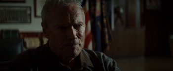 Movie still from “Gran Torino” (2008), directed by Clint Eastwood – An older man sitting in front of an american flag; Close Up shot, Low angle
