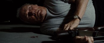 Movie still from “Gran Torino” (2008), directed by Clint Eastwood – A man laying on the ground holding a bottle of wine; Close Up shot, Overhead angle