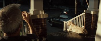 Movie still from “Gran Torino” (2008), directed by Clint Eastwood – A dog sitting on the steps next to a parked car; Wide shot, Over the shoulder angle