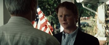 Movie still from “Gran Torino” (2008), directed by Clint Eastwood – A man standing next to another man in front of an american flag; Close Up shot, Over the shoulder angle