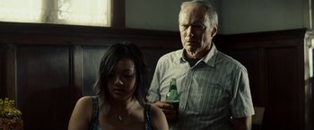 Movie still from “Gran Torino” (2008), directed by Clint Eastwood – An older man holding a bottle of beer next to a young woman; Medium shot, Low angle
