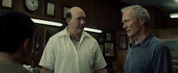Movie still from “Gran Torino” (2008), directed by Clint Eastwood – Two men standing next to each other in front of a wall; Medium shot, Over the shoulder angle