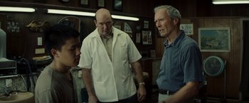 Movie still from “Gran Torino” (2008), directed by Clint Eastwood – A man in a white lab coat standing next to two other men; Medium shot, Over the shoulder angle