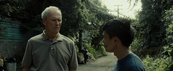 Movie still from “Gran Torino” (2008), directed by Clint Eastwood – A man standing next to another man on a street; Close Up shot, Over the shoulder angle