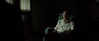 Movie still from “Gran Torino” (2008), directed by Clint Eastwood – An older man sitting in a chair in a dark room; Medium shot, High angle
