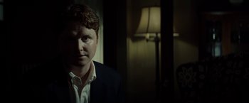 Movie still from “Gran Torino” (2008), directed by Clint Eastwood – A man wearing a suit and tie in a dark room; Close Up shot, Over the shoulder angle