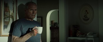 Movie still from “Gran Torino” (2008), directed by Clint Eastwood – An older man holding a coffee cup in a dark room; Medium shot, Over the shoulder angle