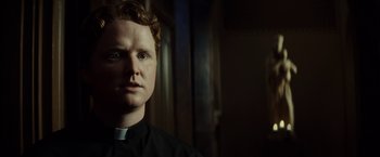 Movie still from “Gran Torino” (2008), directed by Clint Eastwood – A man wearing a priest's collar is looking at the camera; Close Up shot, Low angle