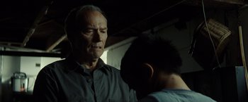 Movie still from “Gran Torino” (2008), directed by Clint Eastwood – An older man and a younger man are standing in a dark room; Close Up shot, Low angle