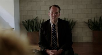 Movie still from “Grandma” (2015), directed by Paul Weitz – A man in a suit and tie sitting in front of a brick wall; Medium shot, Over the shoulder angle