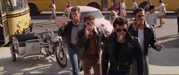 Movie still from “Grease 2” (1982), directed by Patricia Birch – A group of men standing next to each other on a street; Wide shot, Low angle