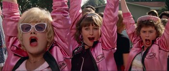 Movie still from “Grease 2” (1982), directed by Patricia Birch – A group of people in pink jackets and a woman in black; Medium shot, Low angle