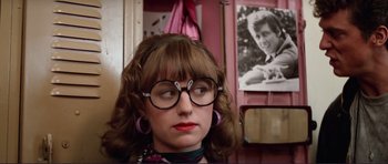 Movie still from “Grease 2” (1982), directed by Patricia Birch – A woman wearing glasses and a bow tie in front of a picture of herself; Close Up shot, Over the shoulder angle
