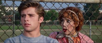 Movie still from “Grease 2” (1982), directed by Patricia Birch – A man and a woman standing next to each other behind barbed wire; Close Up shot, Over the shoulder angle