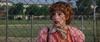 Movie still from “Grease 2” (1982), directed by Patricia Birch – A woman in a pink jacket standing behind a fence; Close Up shot, Over the shoulder angle