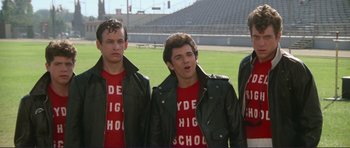 Movie still from “Grease 2” (1982), directed by Patricia Birch – A group of men standing next to each other on top of a football field; Medium shot, Low angle