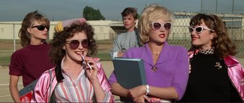Movie still from “Grease 2” (1982), directed by Patricia Birch – Two women and a man are standing in a parking lot; Medium shot, Over the shoulder angle