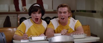 Movie still from “Grease 2” (1982), directed by Patricia Birch – A man and a woman sitting in front of a cake; Medium shot, Low angle